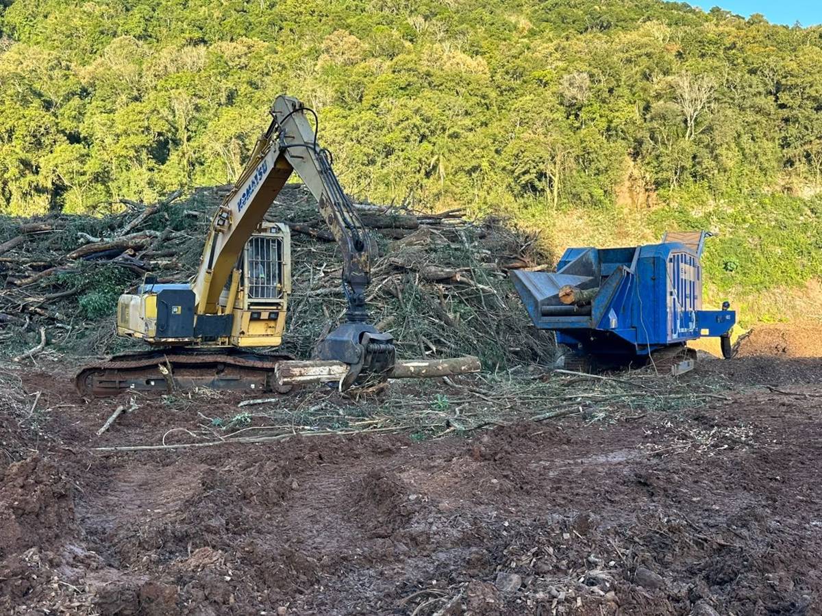 Escavadeira com garra alimentando triturador de biomassa